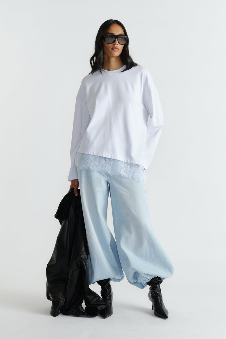Woman wearing a relaxed white long-sleeve top with lace trim paired with wide-leg light denim jeans and black boots