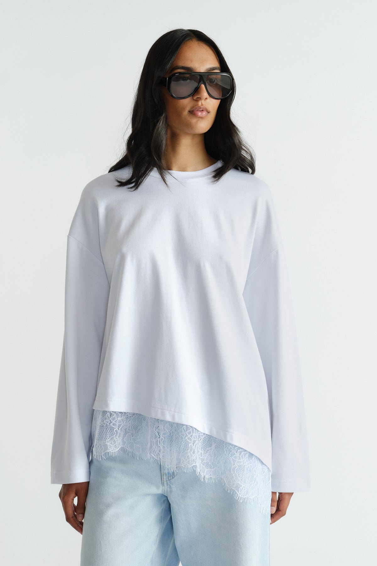 Woman wearing relaxed white long sleeve top with delicate lace trim and light wash denim jeans and oversized sunglasses