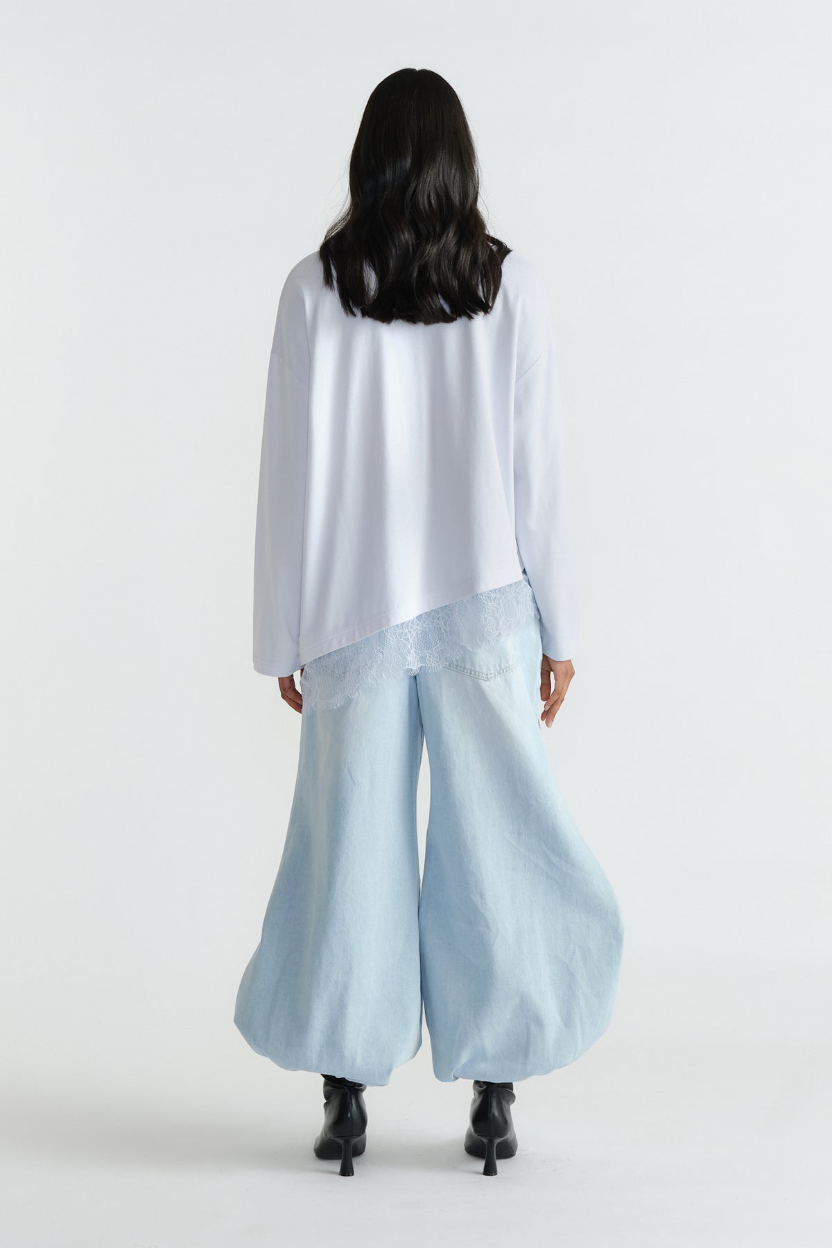 Back view of a long-sleeve top with delicate lace trim paired with light wide-leg denim pants and black boots.