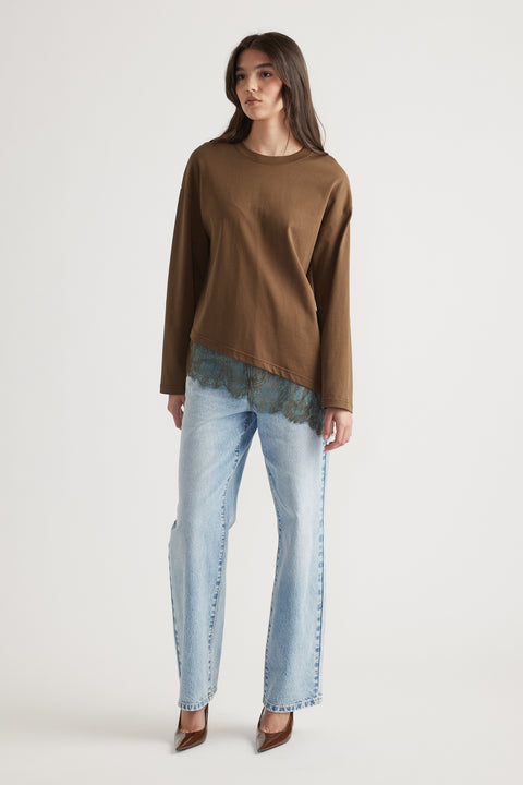 Woman wearing a brown long sleeve top with lace trim layered over light wash straight-leg jeans and brown heels