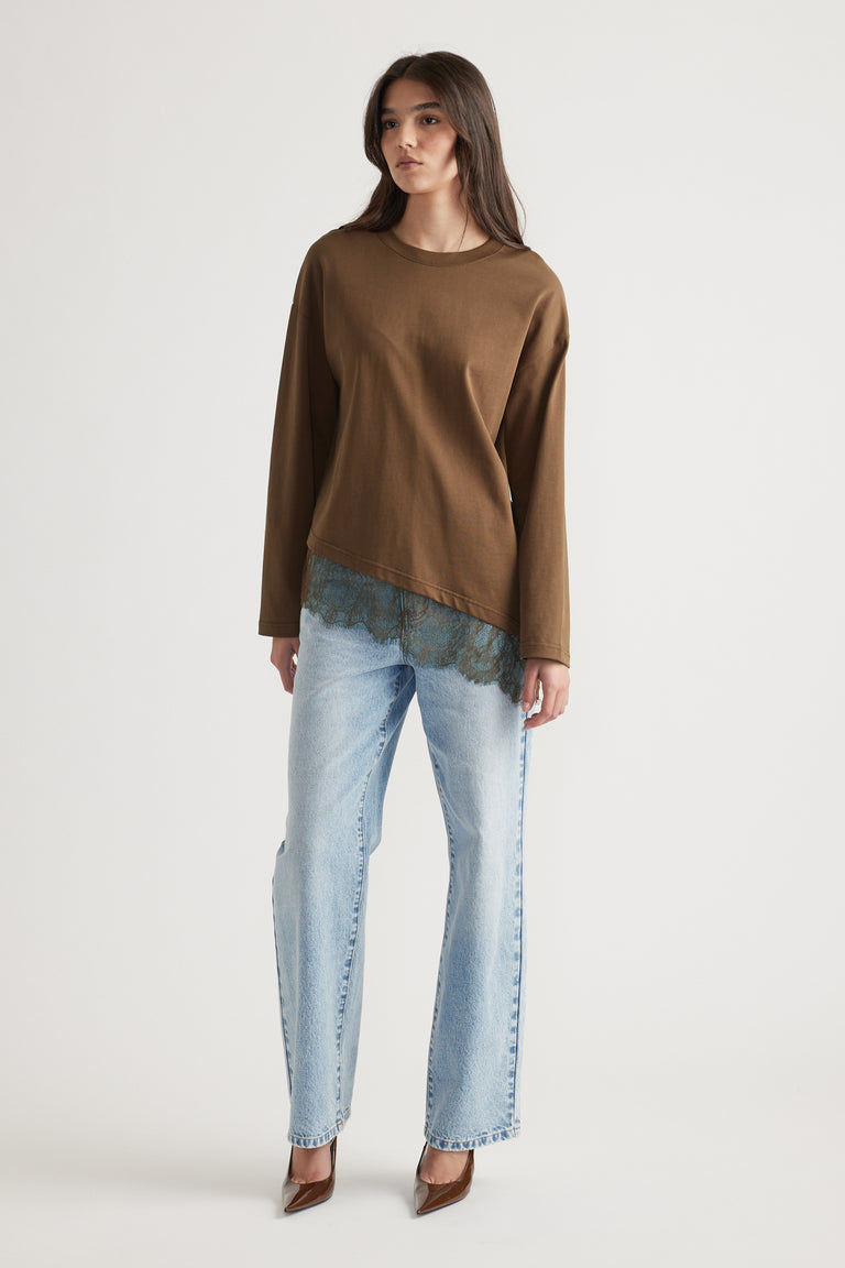 Woman wearing a brown long sleeve top with lace trim layered over light wash straight-leg jeans and brown heels