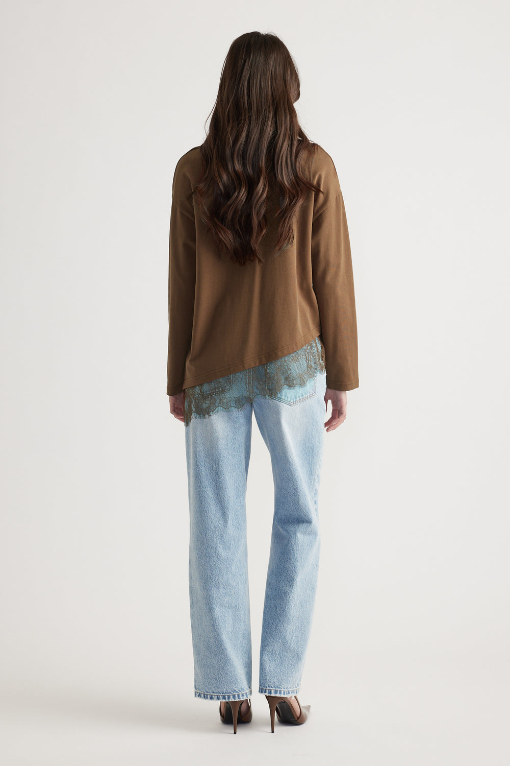 Woman with long wavy hair wearing a brown long sleeve top with lace trim paired with light wash straight jeans and heels