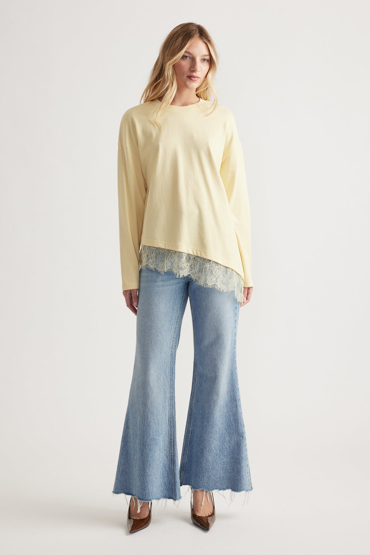 Woman wearing a pale yellow long-sleeve top with lace trim, paired with light-wash flared jeans and brown pointed heels