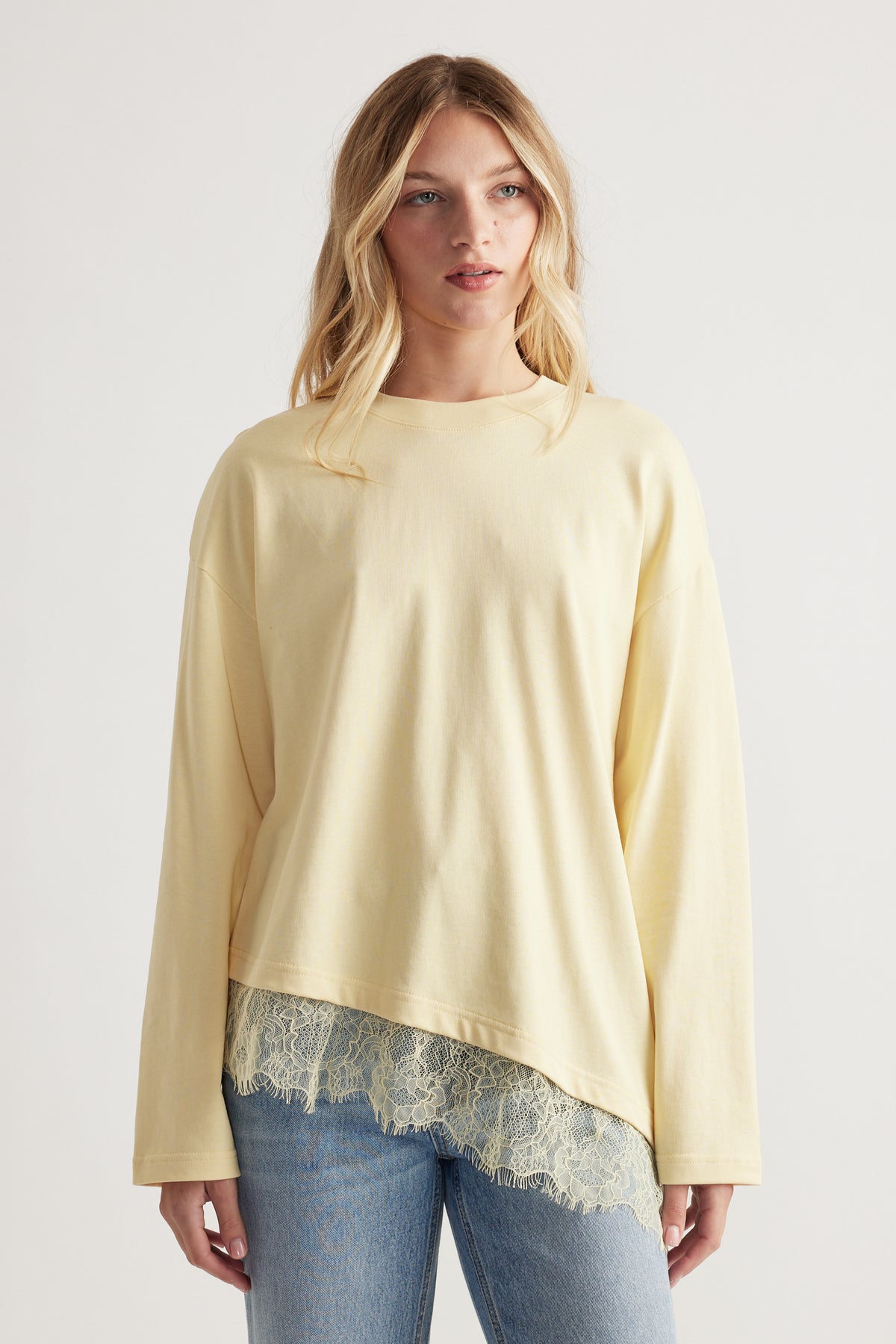 Woman wearing a soft yellow long-sleeve top with lace trim hem paired with light wash denim jeans