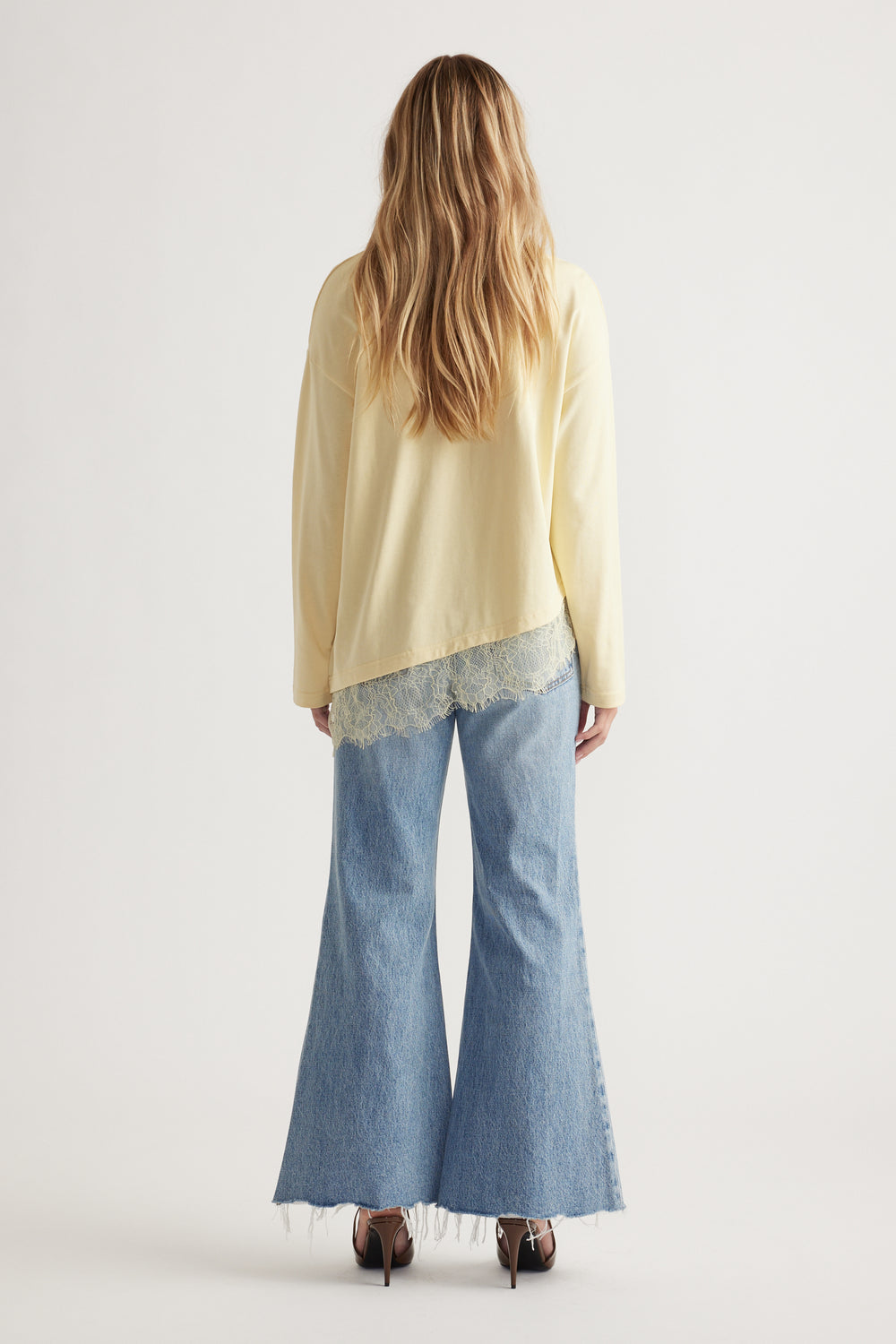 Woman wearing a pale yellow long sleeve top with lace trim paired with light blue wide-leg raw-hem jeans and heels