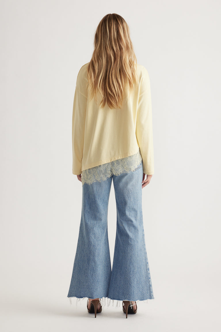 Woman wearing a pale yellow long sleeve top with lace trim paired with light blue wide-leg raw-hem jeans and heels