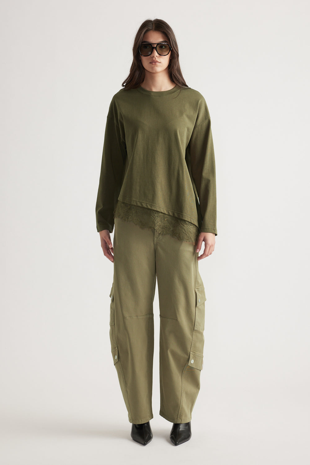 Woman wearing olive long-sleeve top with lace trim paired with relaxed cargo pants and black pointed boots.