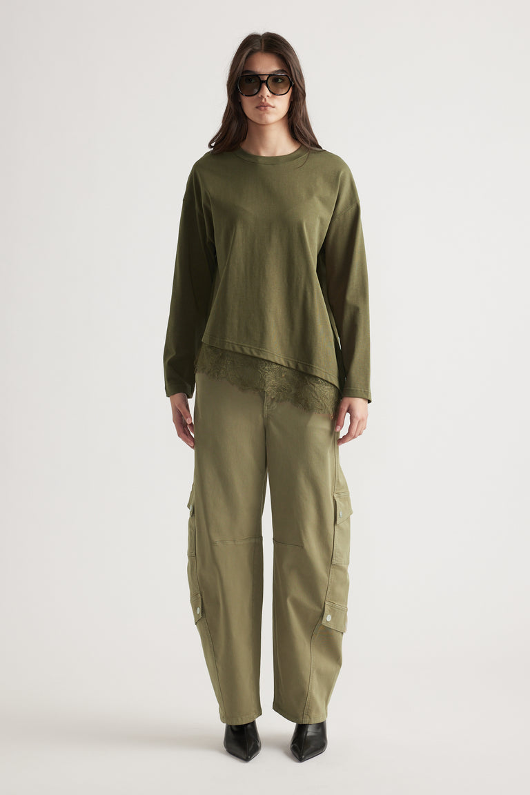 Woman wearing olive long-sleeve top with lace trim paired with relaxed cargo pants and black pointed boots.