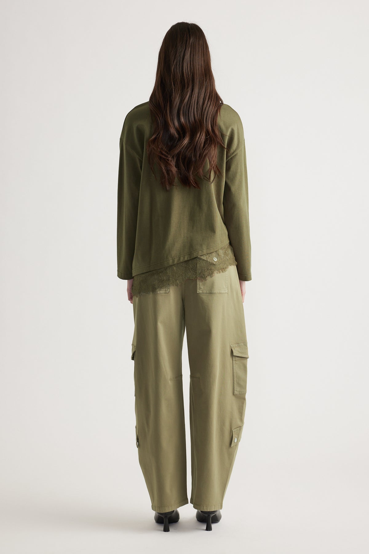 Woman wearing olive long sleeve top with lace trim and matching relaxed cargo pants with black heeled boots viewed from behind