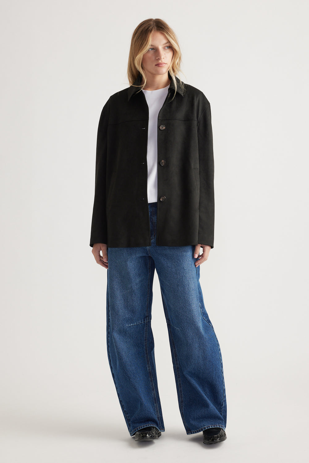 Woman wearing a relaxed black buttoned coat over a white top paired with wide-leg blue denim jeans and black shoes