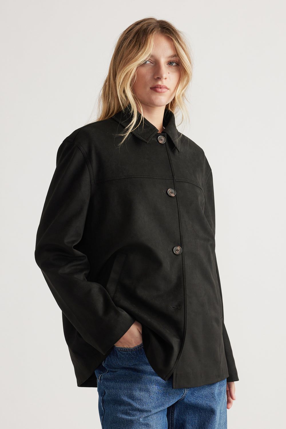 Woman wearing a loose black coat with button closure paired with relaxed blue denim jeans against a plain background