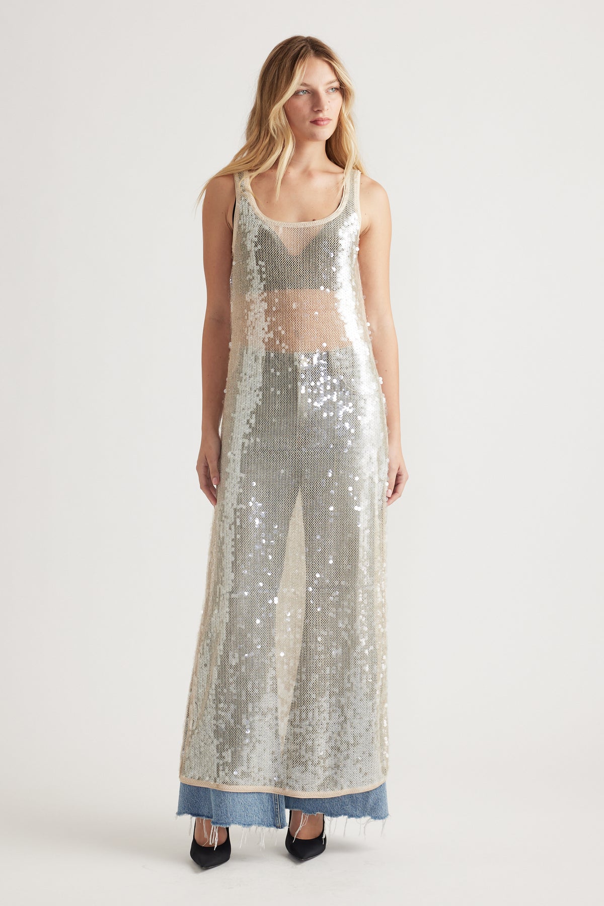 Woman wearing a sleeveless silver sequin maxi dress layered over casual denim jeans and black pointed heels