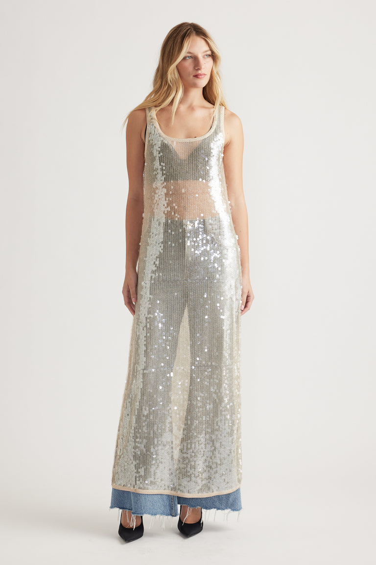 Woman wearing a sleeveless silver sequin maxi dress layered over casual denim jeans and black pointed heels