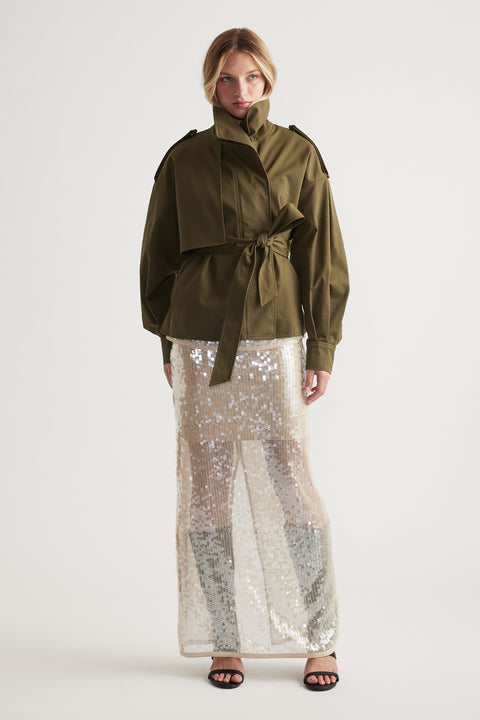 Woman wearing an olive belted jacket paired with a shimmering sequin maxi skirt and black open-toe heels