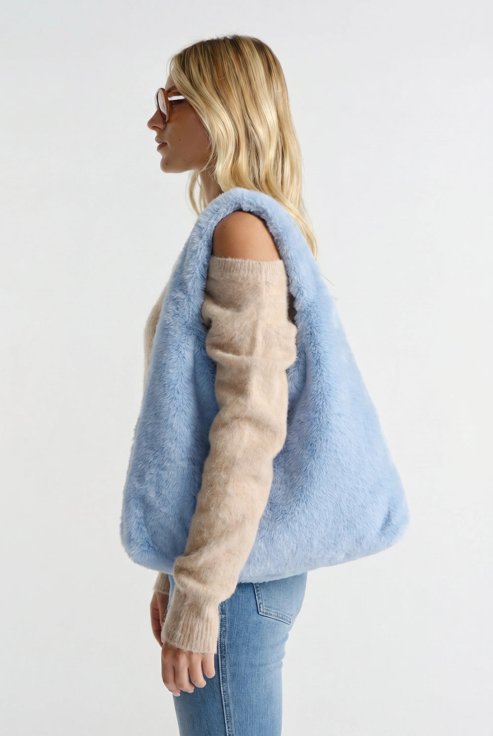 Woman carrying a soft, fluffy pale blue tote bag paired with beige knit sweater and light blue jeans.
