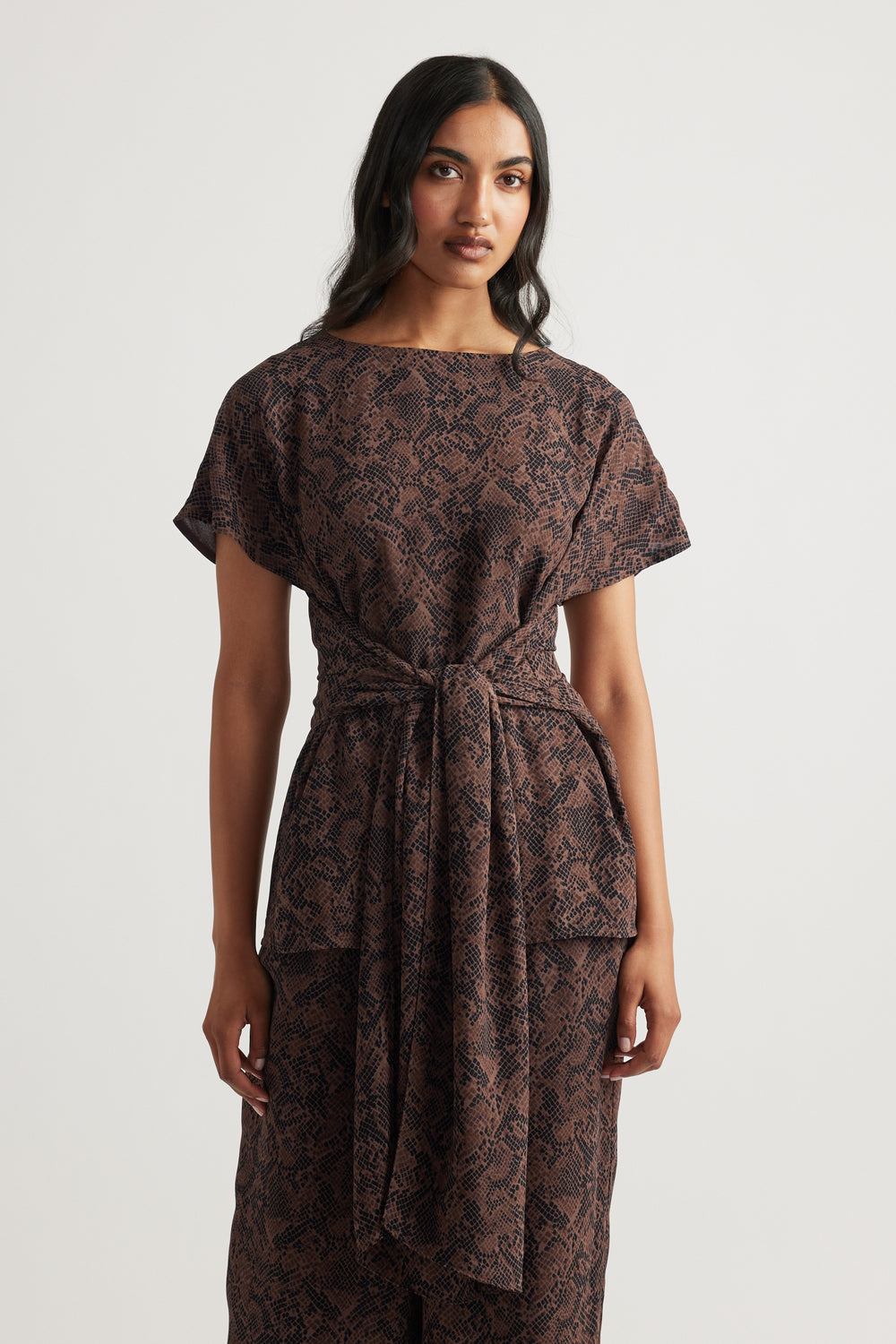 Woman wearing a brown snake-print tie tunic with short sleeves and a relaxed fit, styled for effortless elegance