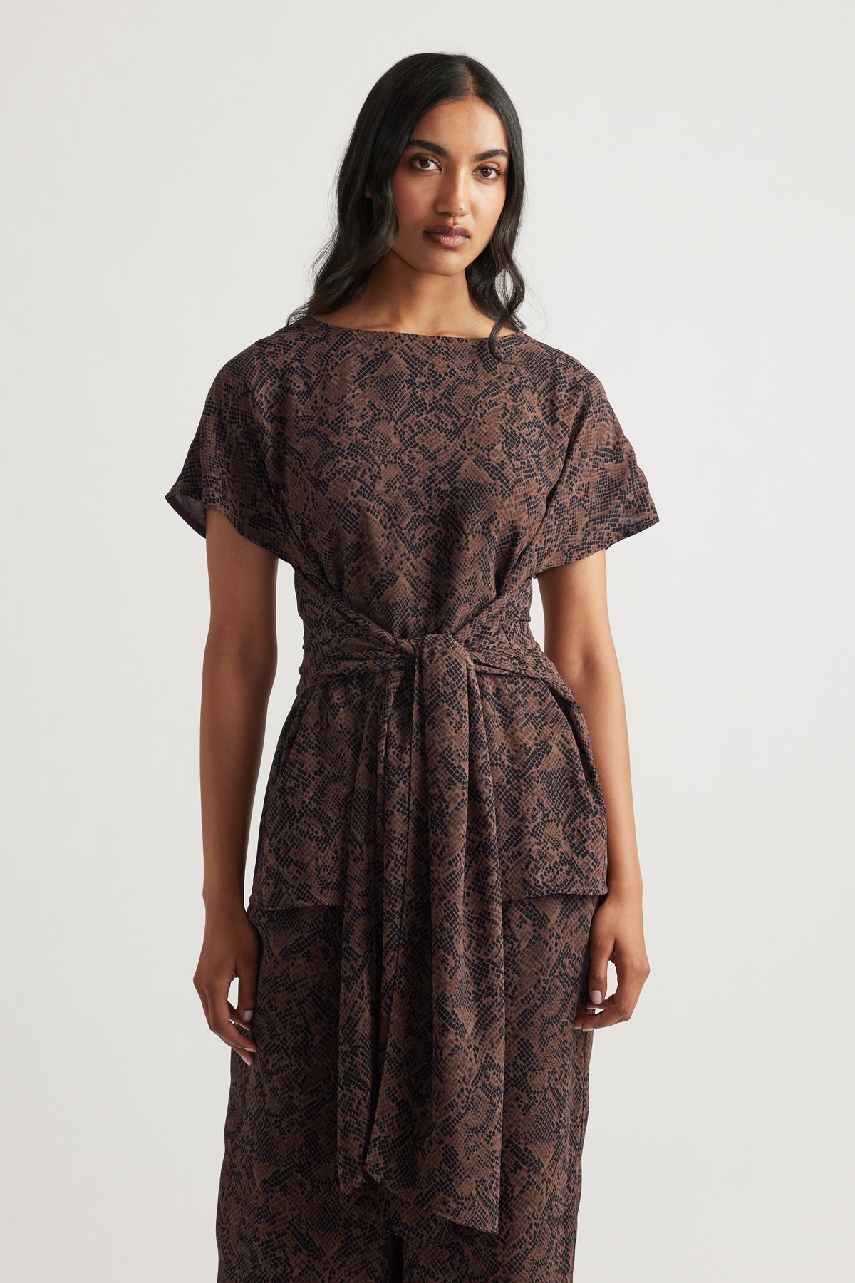 Woman wearing a brown snake-print tie tunic with short sleeves and a relaxed fit, styled for effortless elegance