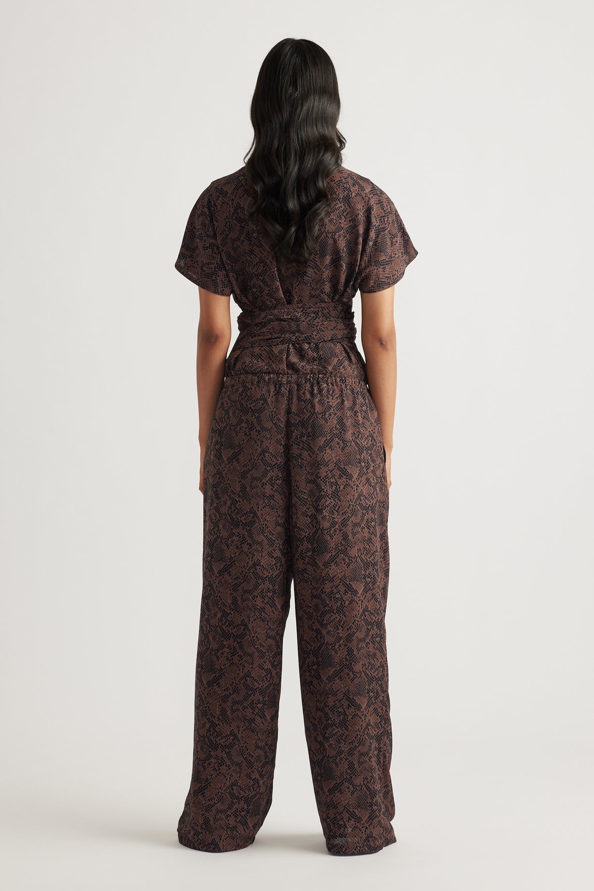 Woman wearing dark snake-print wide-leg pants with a cinched waist and short-sleeve top facing away