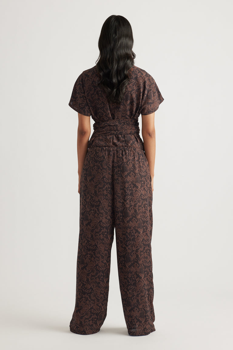 Woman wearing dark snake-print wide-leg pants with a cinched waist and short-sleeve top facing away