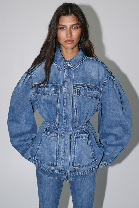 Woman wearing a cinched blue denim jacket with a collared neckline front pockets and matching jeans