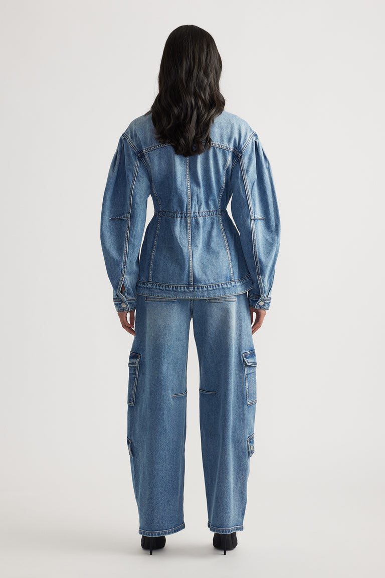 Rear view of a woman wearing a tailored cinched denim jacket paired with relaxed fit cargo denim pants and black heels