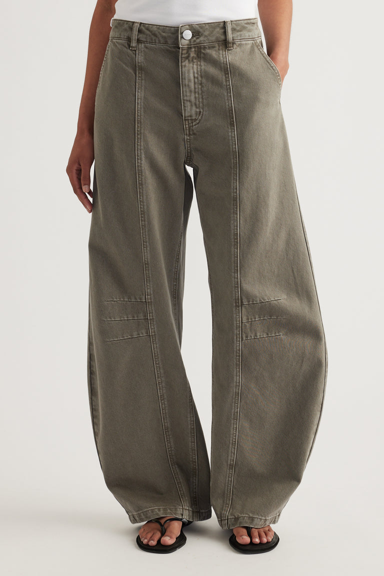 Woman wearing high rise olive barrel leg jeans with front seams and knee darts, paired with a white top and sandals