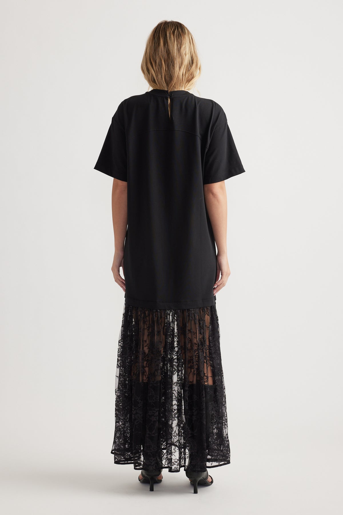 Rear view of woman wearing black short sleeve dress with a solid top and sheer spliced lace maxi skirt panel