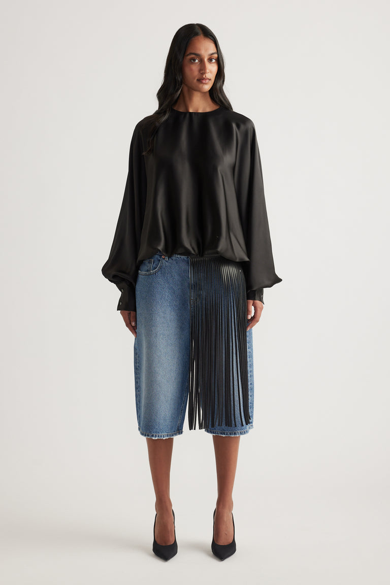 Model wearing a black satin top with balloon sleeves and an elasticated hem, styled with denim