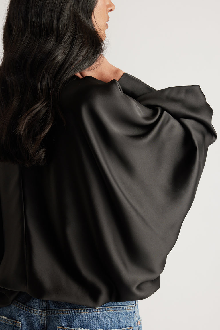 Model wearing a black satin top with balloon sleeves and a bubble hem, paired with blue jeans