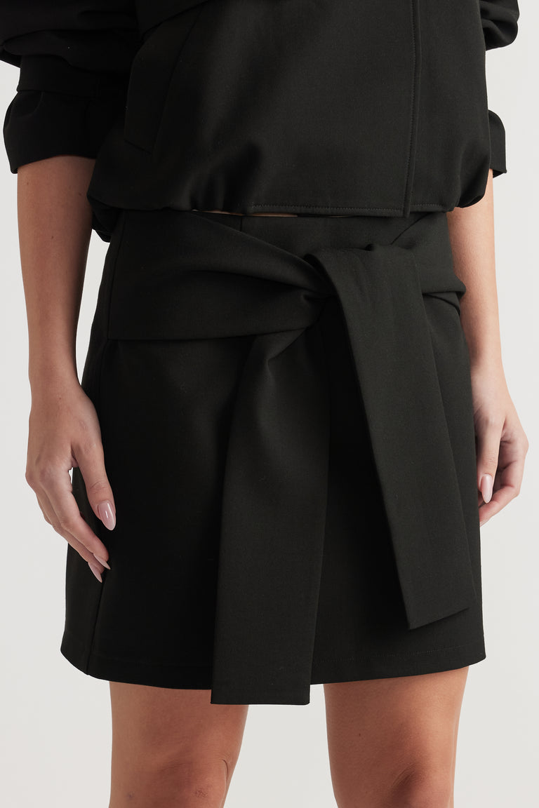 Black mini skirt with mid-rise waist and wide tie detail, paired with matching top on light background