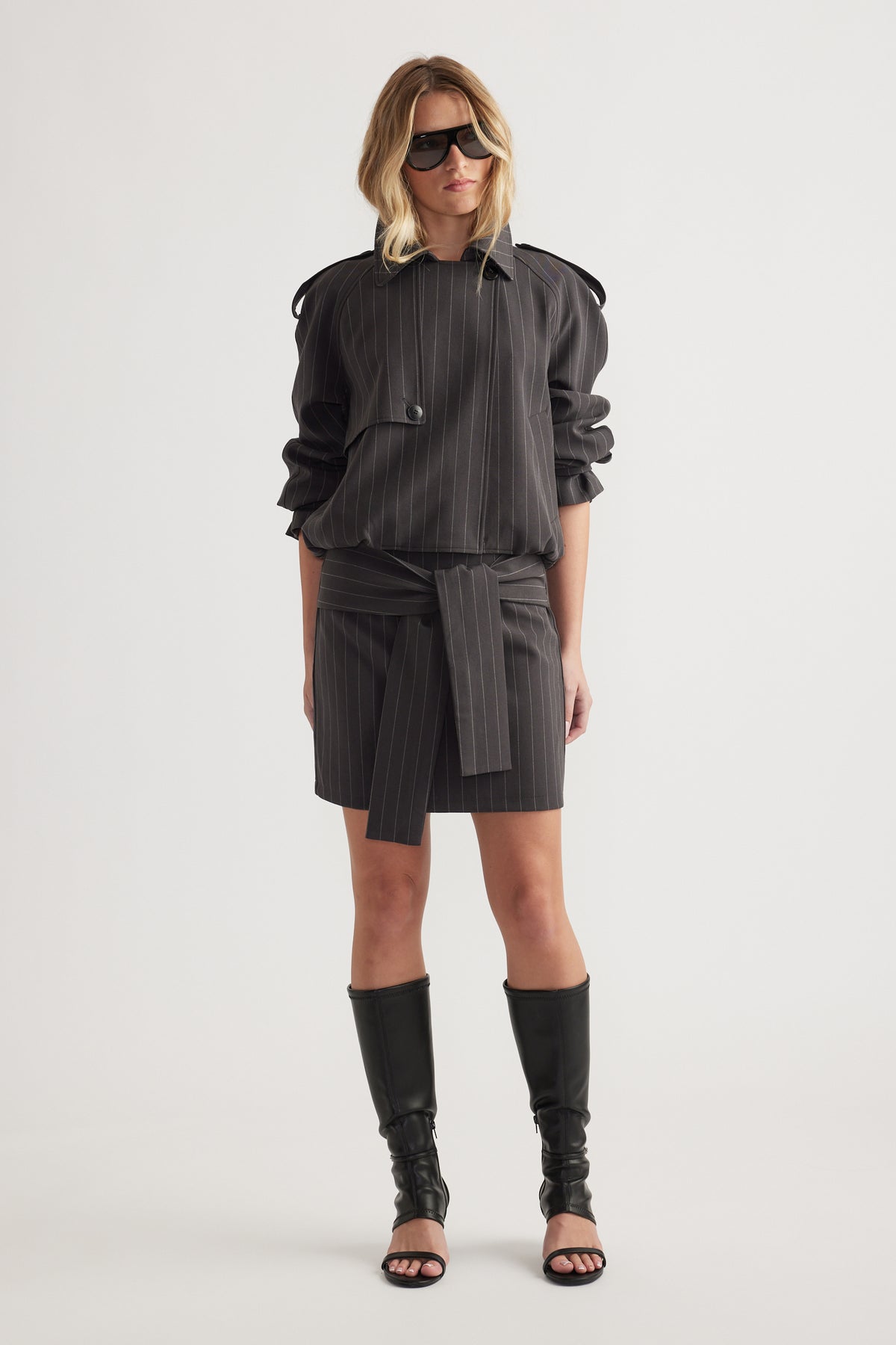 Woman wearing a dark pinstripe mini skirt with a matching long sleeve top and black knee-high boots