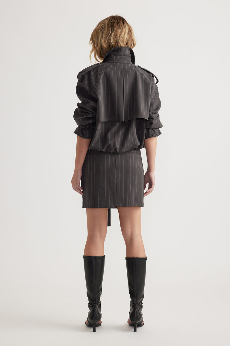 Rear view of woman wearing a dark pinstripe mini skirt paired with a matching jacket and knee-high black boots