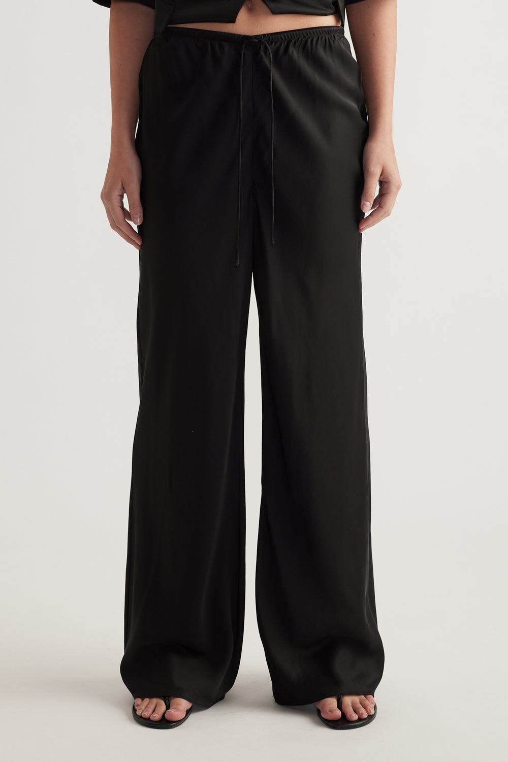 Model wearing black full length pants with a wide leg and elastic drawcord waist
