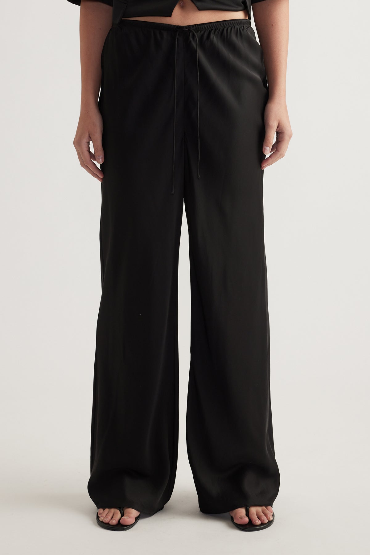 Model wearing black full length pants with a wide leg and elastic drawcord waist