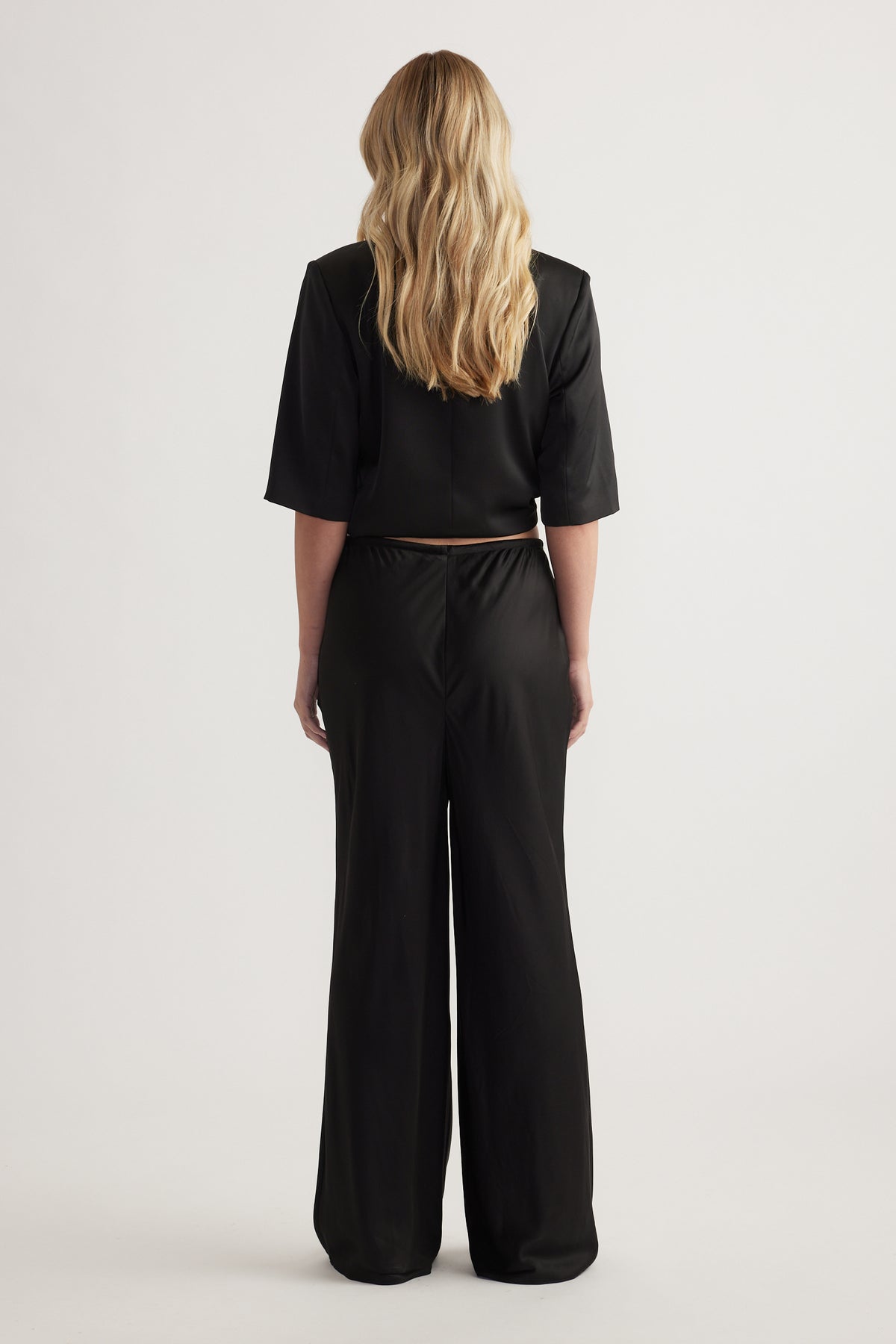 Back view of a model wearing black full length straight leg pants with an elasticated waist