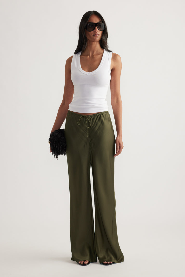 Model wearing olive green full length straight leg pants with a drawcord waist and white tank top
