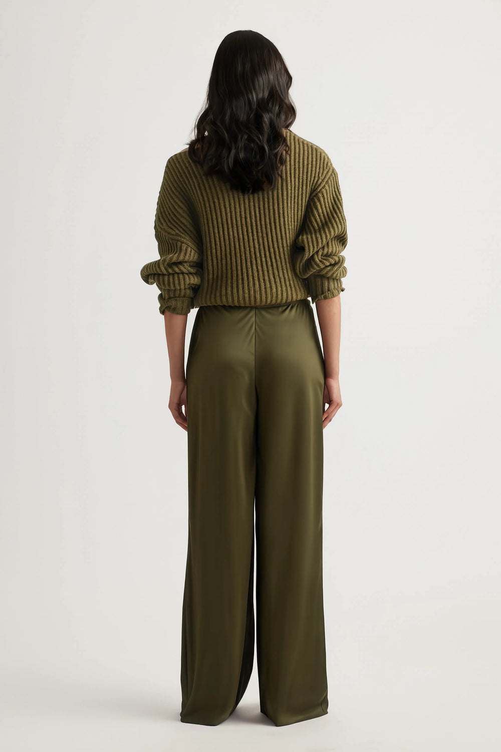 Back view of a woman wearing olive bias-cut straight-leg pants with an elastic waist and ribbed sweater