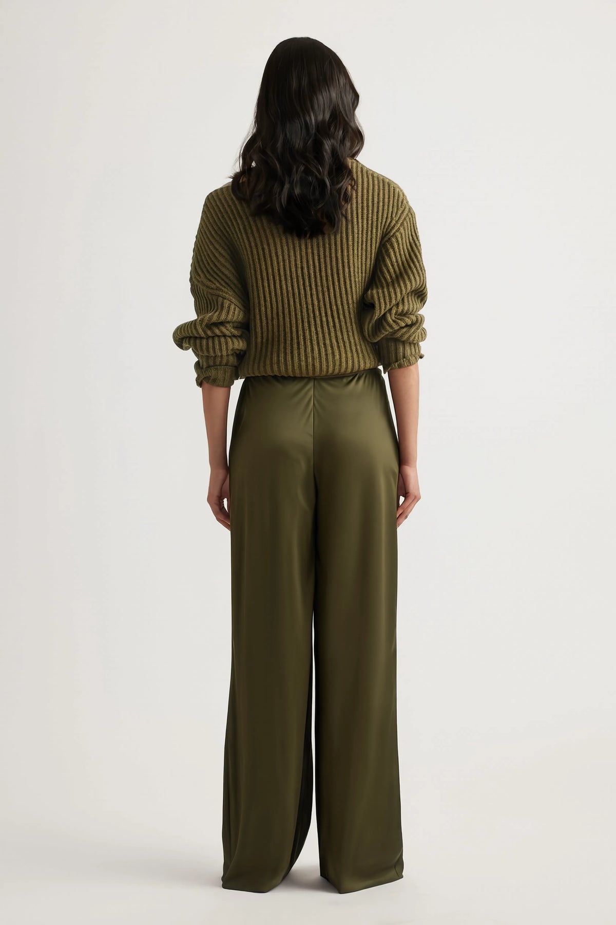 Back view of a woman wearing olive bias-cut straight-leg pants with an elastic waist and ribbed sweater