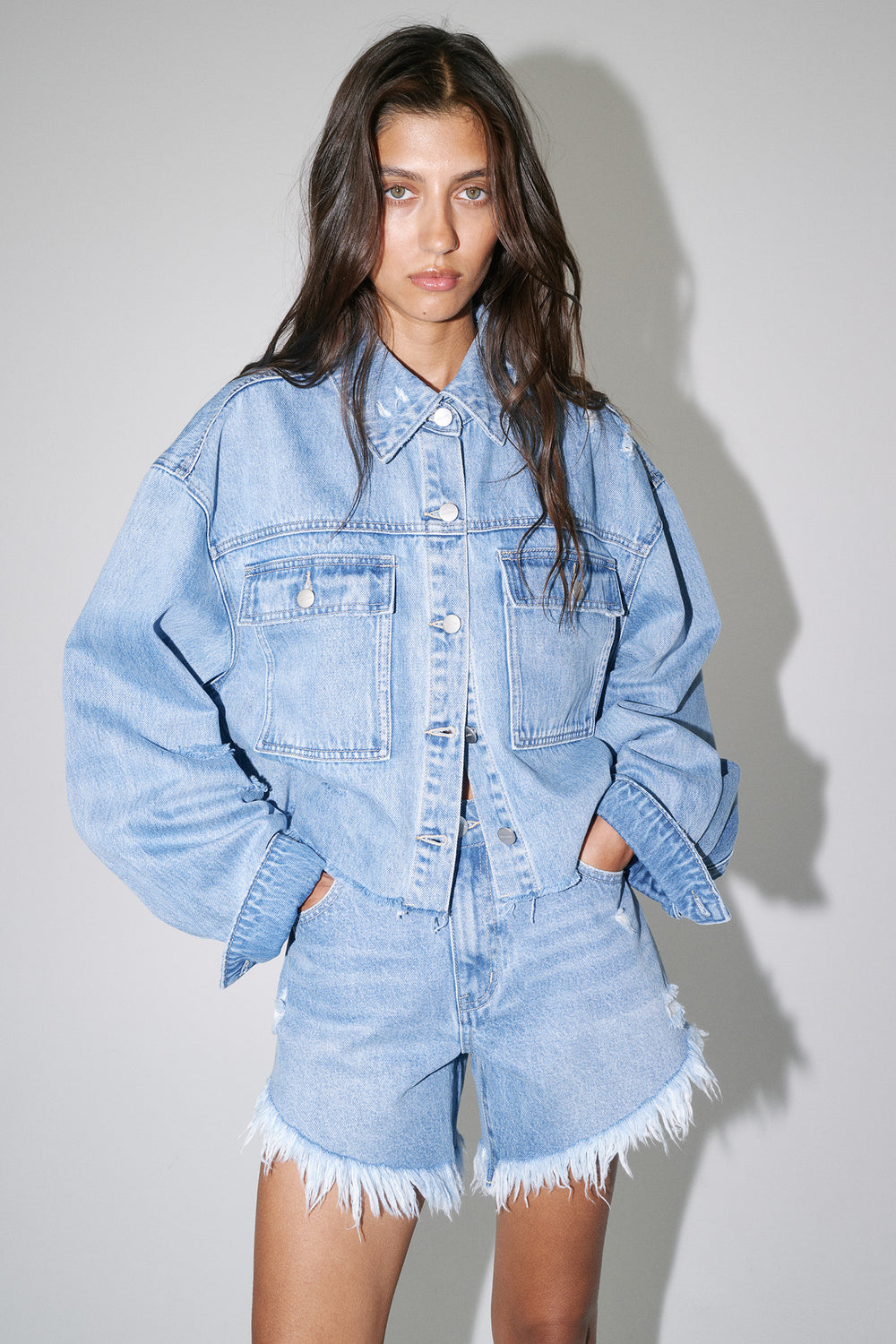 Model wearing a light wash cropped denim shirt with patch pockets and matching frayed shorts