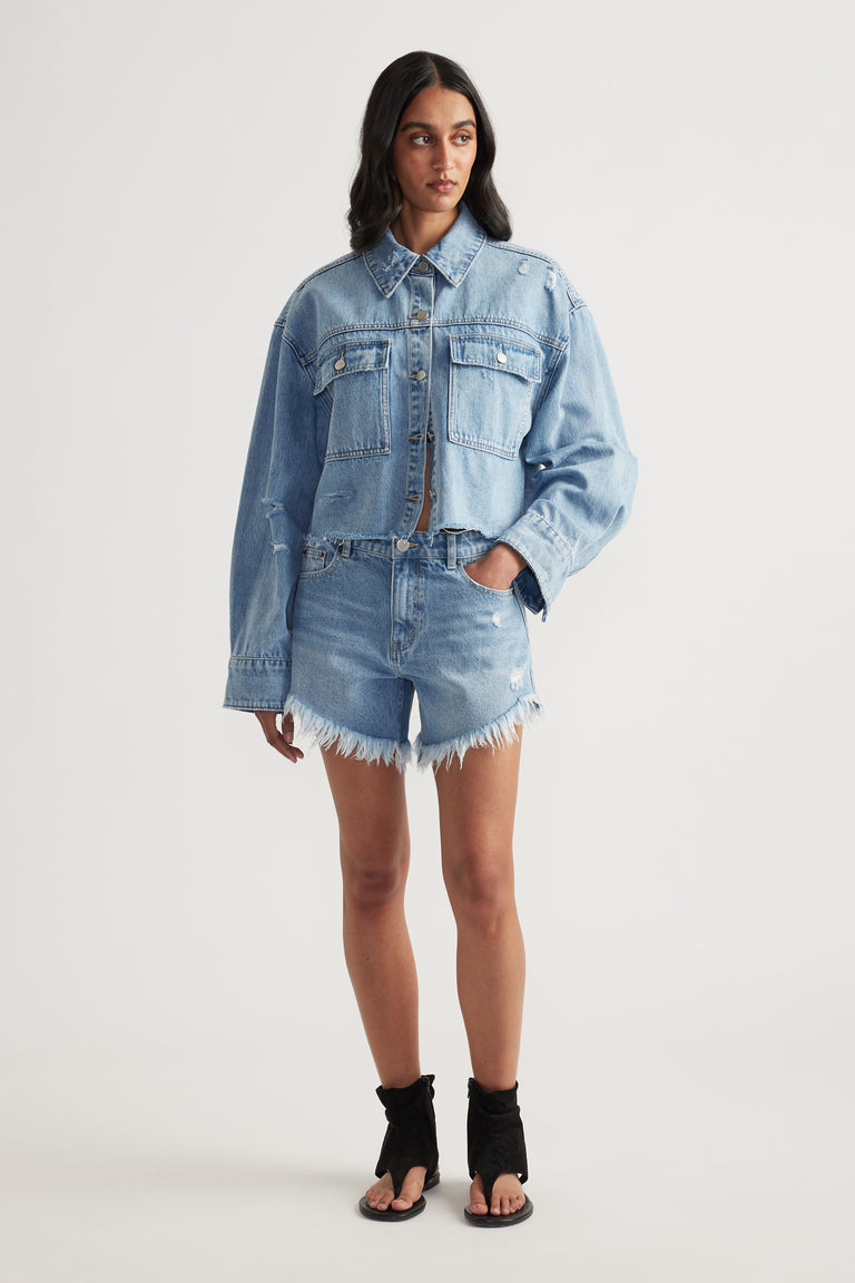 Woman in a light wash denim shirt with patch pockets and distressed frayed denim shorts with black heeled sandals