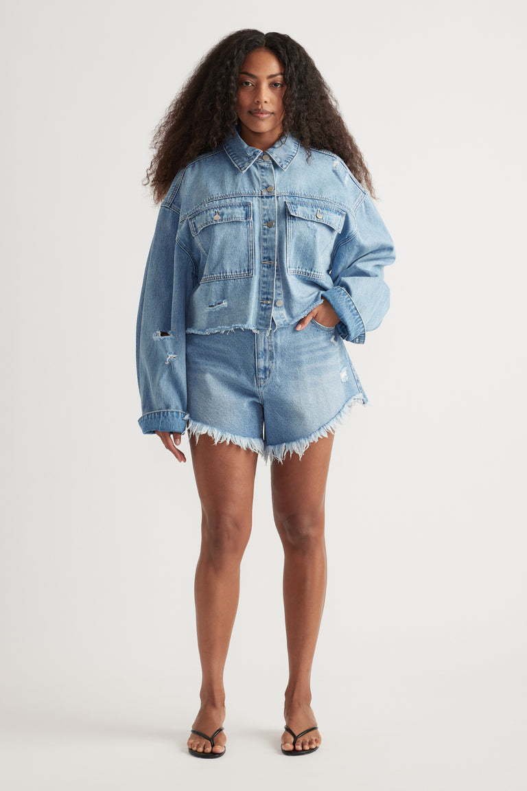 Woman wearing a cropped light blue distressed denim shirt with matching frayed shorts and sandals