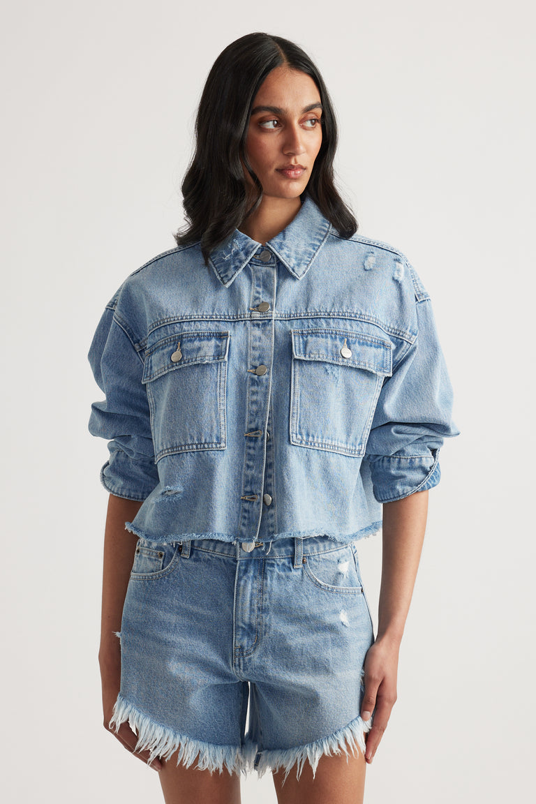 Woman wearing a cropped light wash denim shirt with patch pockets and frayed denim shorts