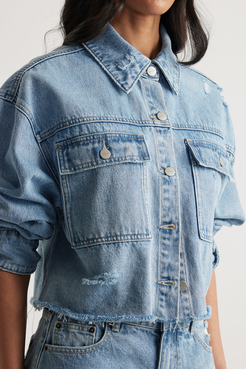 Woman wearing a light wash cropped denim shirt with distressed details and patch pockets