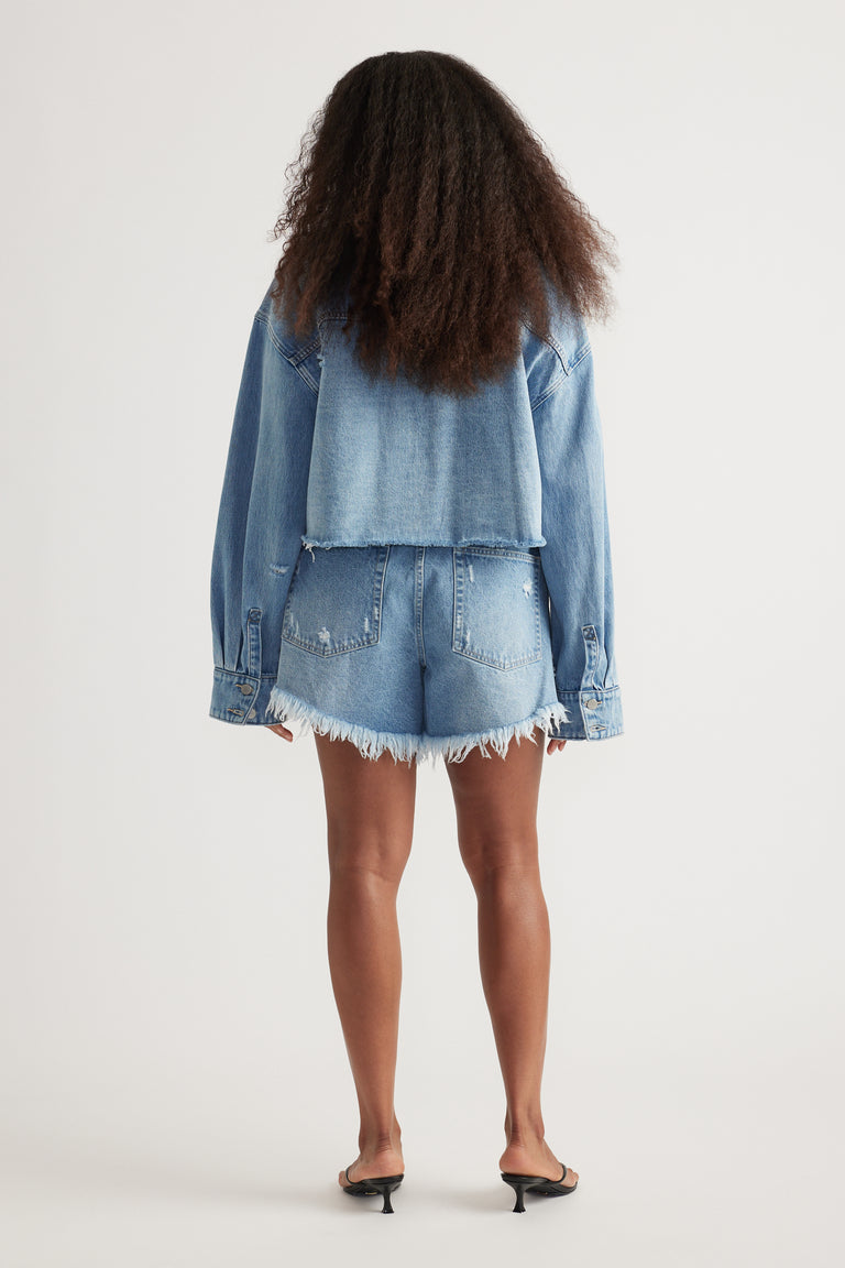 Back view of a woman wearing a cropped denim shirt with frayed denim shorts and black heeled sandals