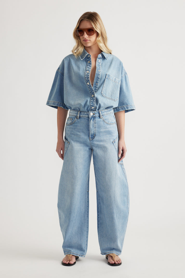 Woman in light wash barrel-leg jeans and a short-sleeve denim shirt with sunglasses