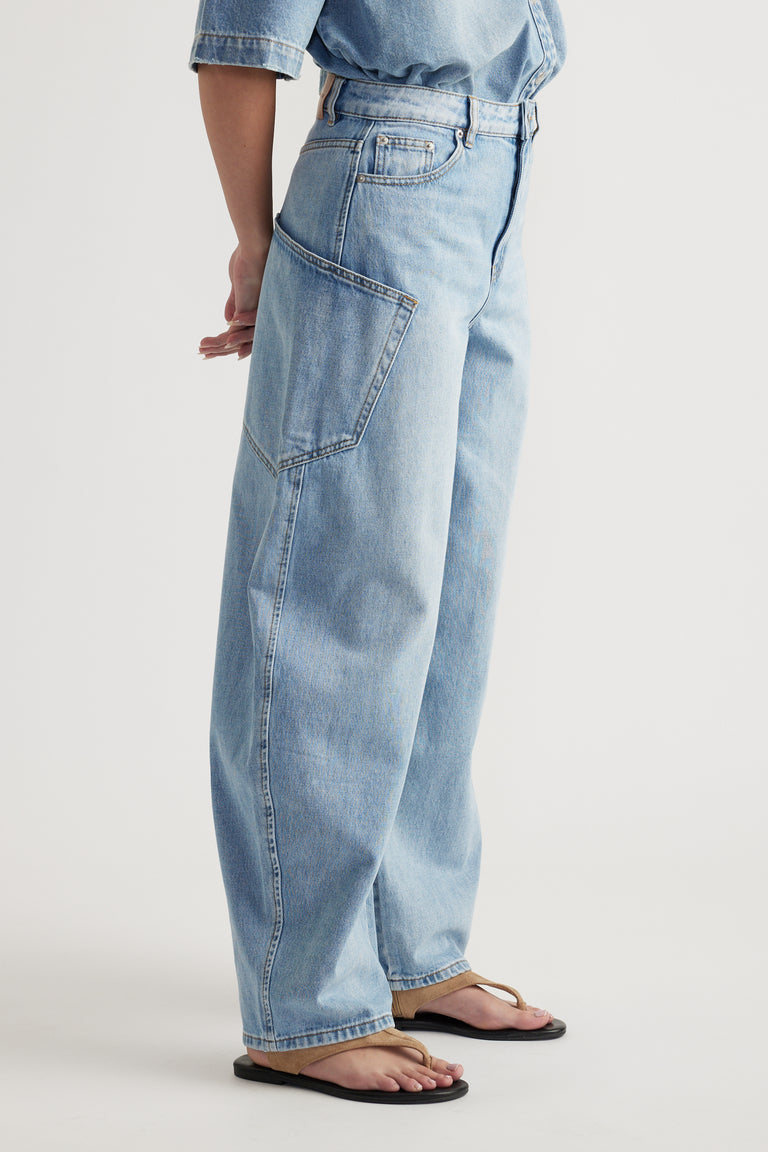 Side view of model wearing light wash barrel jeans with oversized cargo pockets and flat sandals