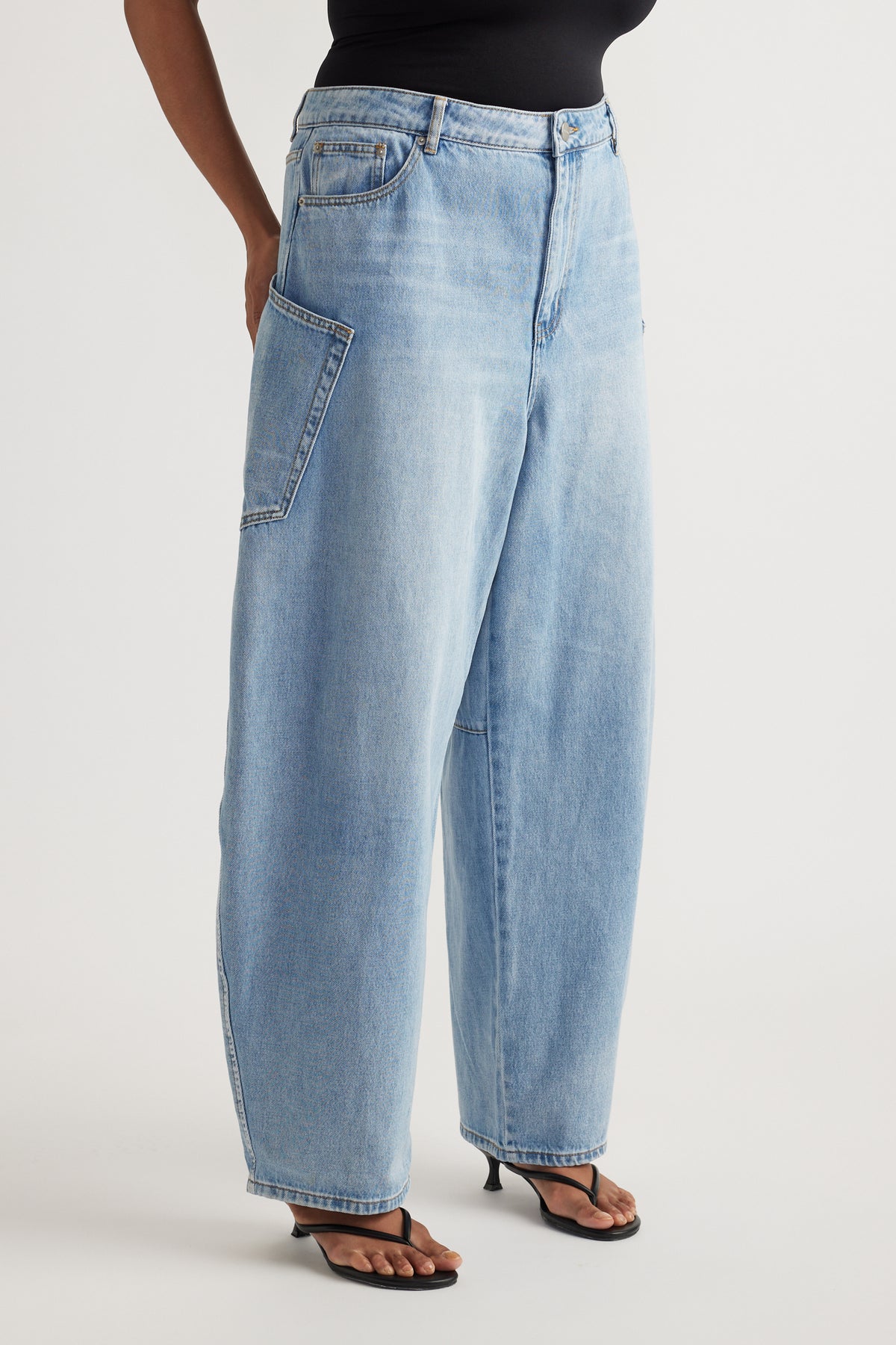 Woman wearing light wash barrel-leg cargo jeans with oversized pockets, a black top and heeled sandals
