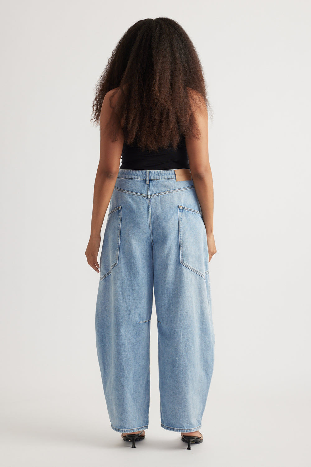 Back view of a woman wearing light wash cargo barrel jeans with oversized pockets and a black sleeveless top