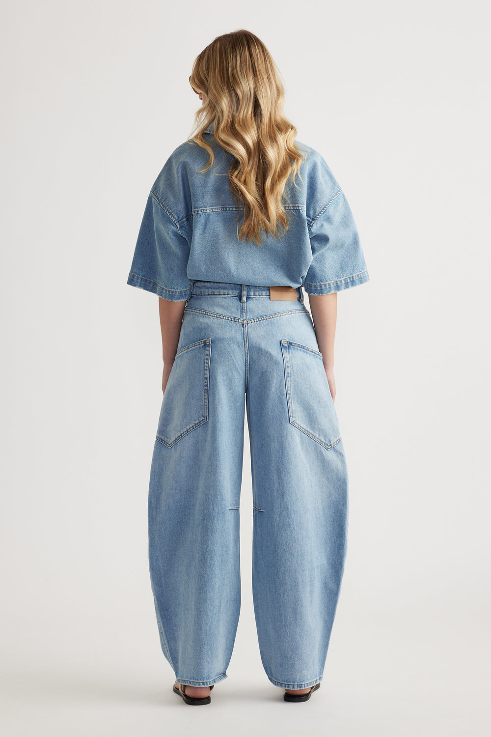 Back view of a woman wearing a cropped denim jacket and light wash cargo barrel jeans