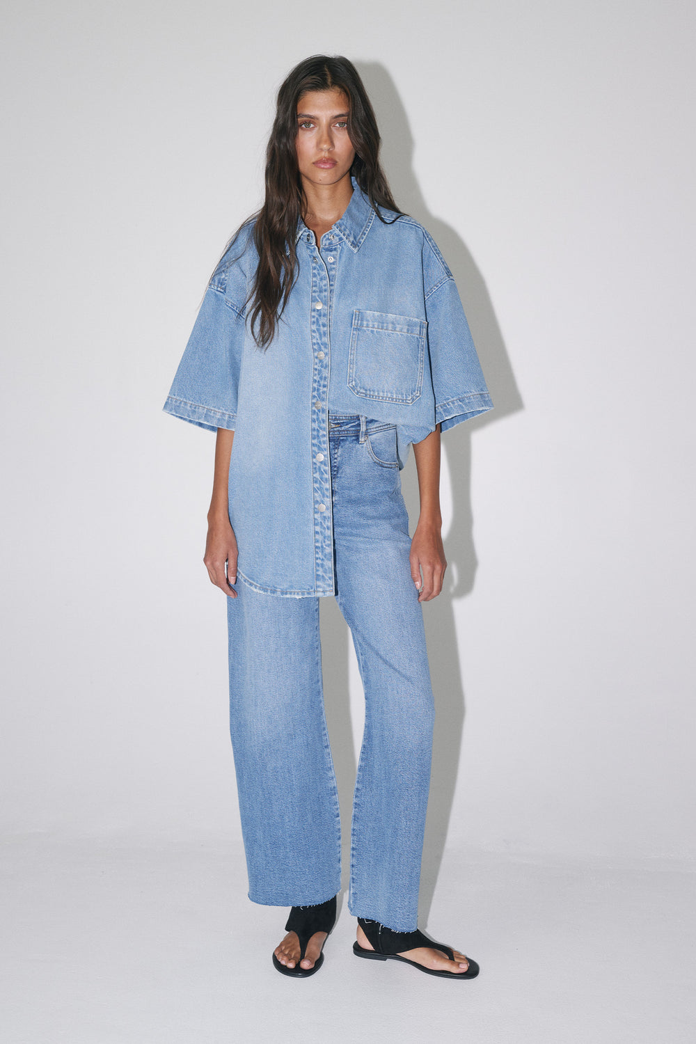 Model wearing an oversized light wash denim shirt with wide leg jeans and black sandals
